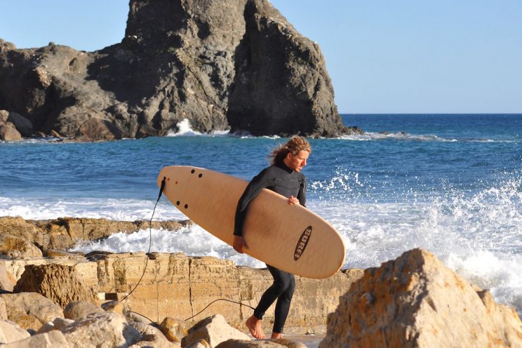 A surfer with wetsuit and board at Black Rock, Praia da Luz