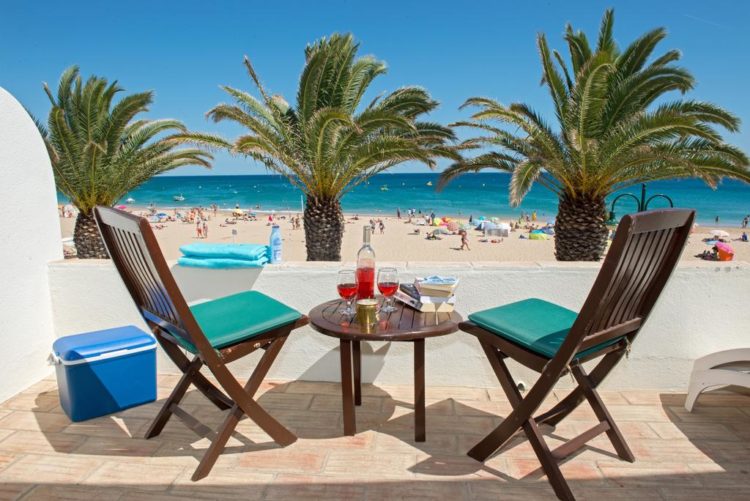 The view from the balcony of Luz Beach Apartments faces the main beach and ocean at Praia da Luz. It features two chairs and a small table