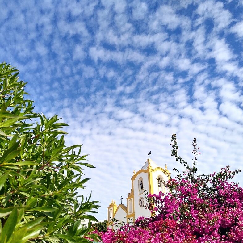Speckled cloud on a blue day above the trees and flowers that surround Luz church